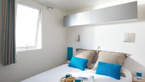 Une chambre à coucher bien rangée, avec un lit, des oreillers, une table de chevet, une fenêtre et un rideau.