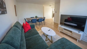 Ein modernes Wohnzimmer mit einem grünen Sofa, einem weißen Couchtisch und einem Fernsehgerät auf einem weißen Schrank.