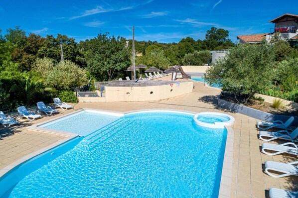 A swimming pool with lounge chairs and a hot tub area surrounded by greenery. - ZEcamping 3 étoiles toboggans locatif TV LV clim 28m2 (Sussargues)