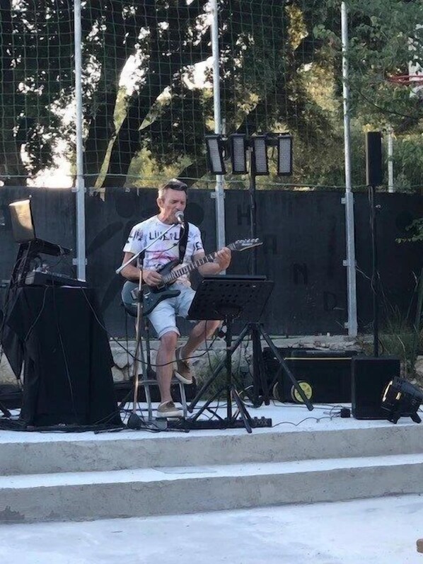 A musician performing on an outdoor stage with a guitar, a music stand, and a microphone.