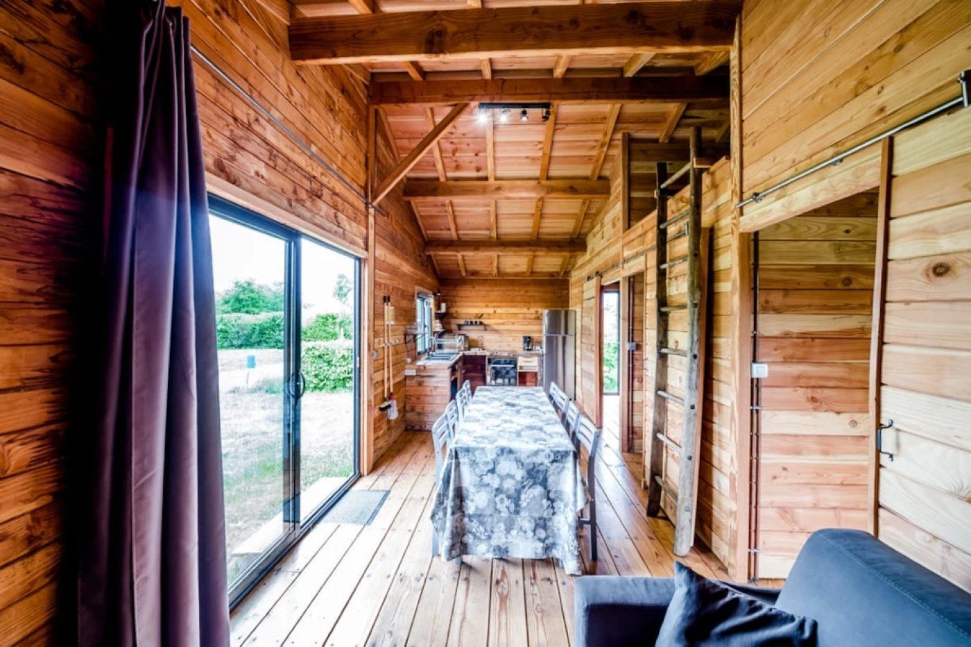 A wooden cabin interior with a dining area, a kitchen, and a large window.