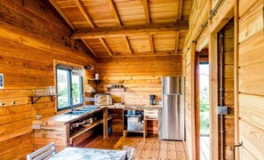 A wooden cabin interior with a kitchen area, including a refrigerator, sink, and wooden cabinets.