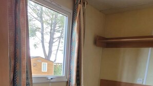 Ein kleines Zimmer mit zwei Etagenbetten, einem Fenster mit Vorhängen und Blick auf ein Gebäude.