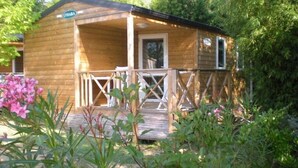 A wooden cabin with a porch, surrounded by greenery and flowering plants.