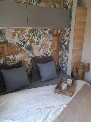 Une chambre à coucher avec un lit, des oreillers, une tête de lit en bois, une décoration en forme de cactus et un plateau avec des tasses.