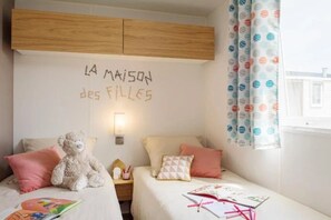 A cozy bedroom with two beds, a teddy bear, and a wall sign reading "LA MAISON des FILLE'S".