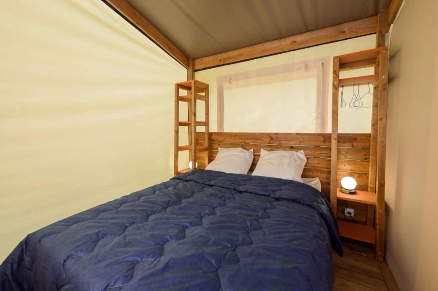 A compact bedroom with a wooden headboard, a single bed with a blue quilt, and a bedside table with a lamp.