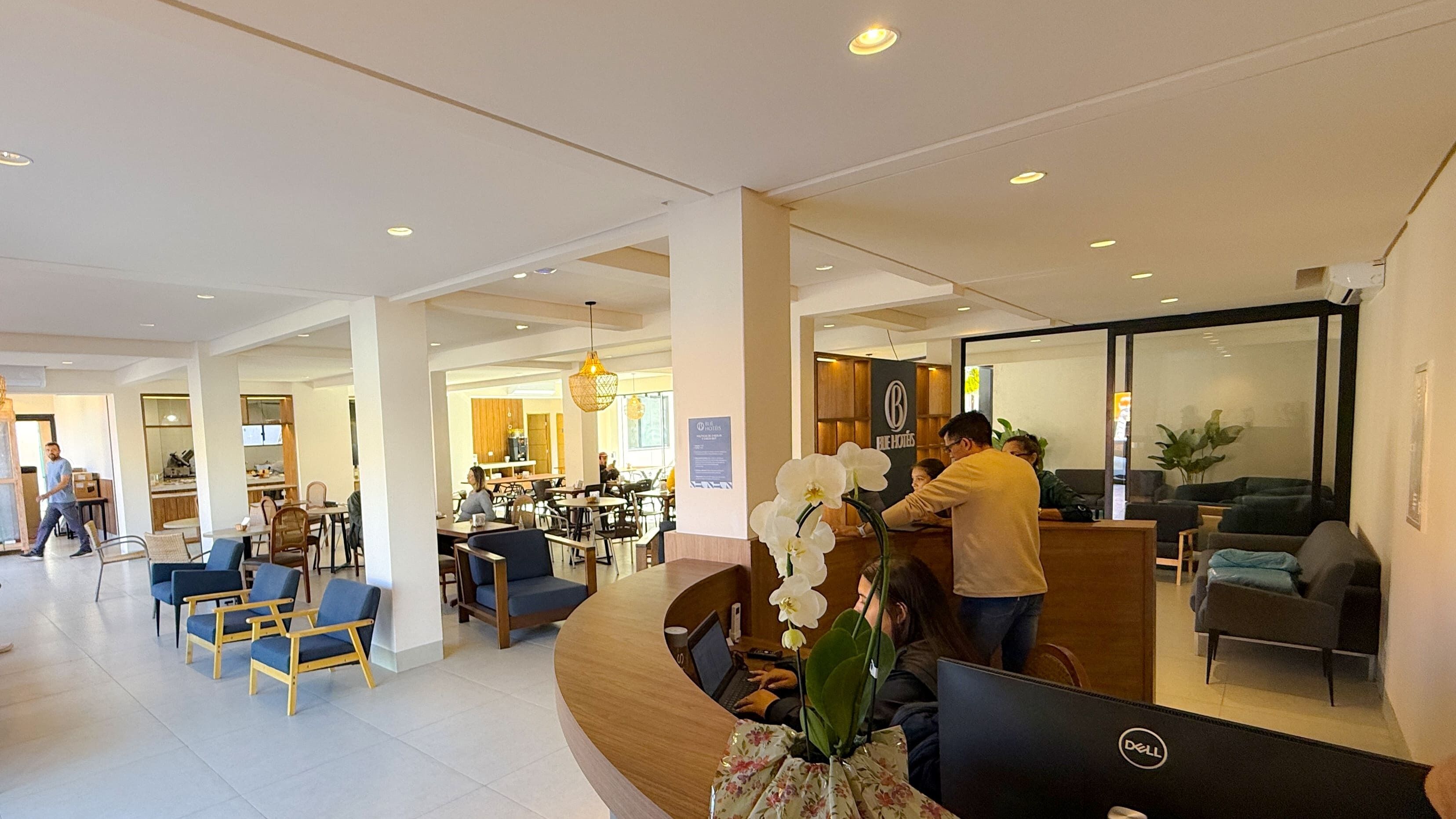 En hotellobby med receptionsdisk, siddeområde og en restaurant i baggrunden.