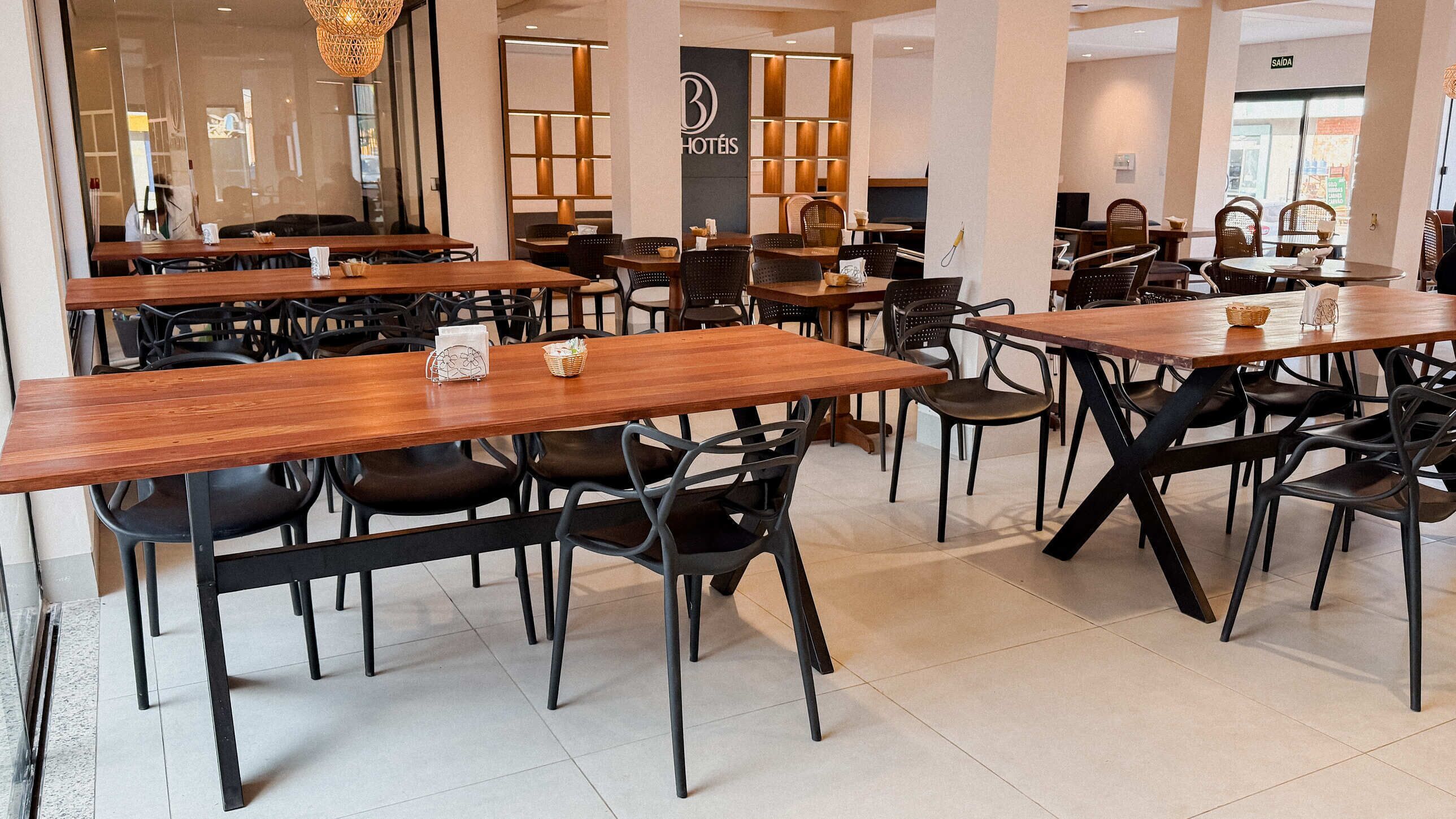 Ristorante di hotel con diversi tavoli in legno e sedie nere, un design d'interni moderno e una segnaletica visibile per l'hotel.