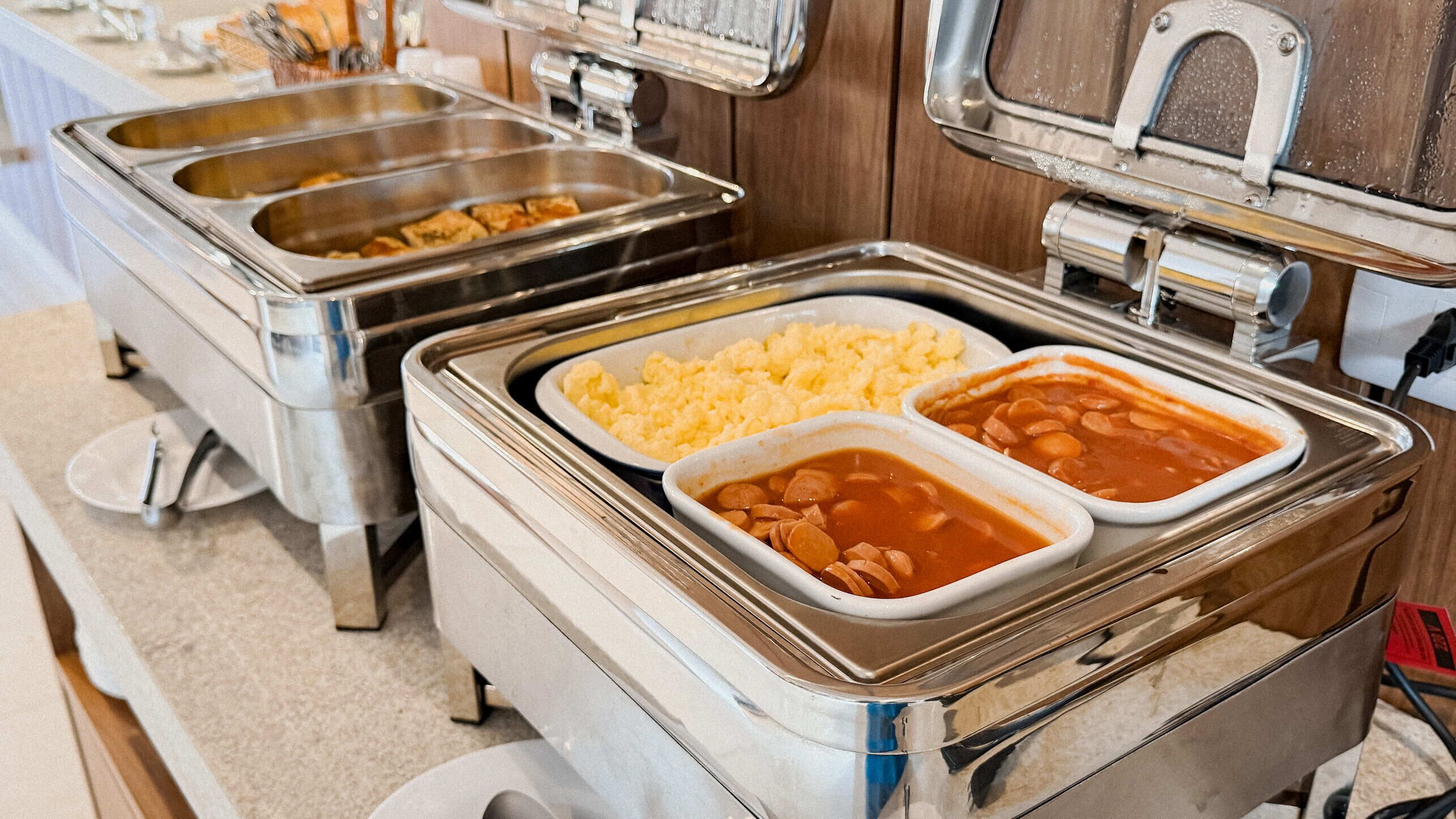 Montaje de bufé con varios recipientes de comida, que parecen huevos revueltos, frijoles y un plato cremoso.