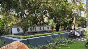 Un jardín ajardinado con un sendero, una roca grande y un muro con detalles decorativos.