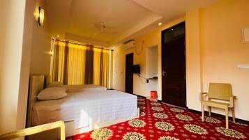 Une chambre d’hôtel avec un lit, une chaise, une moquette rouge à motifs et un téléviseur fixé au mur.