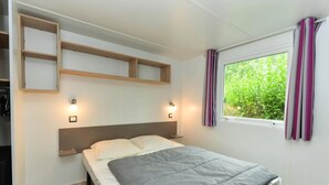 Ein Schlafzimmer mit einem Bett, zwei Nachttischen, einem Fenster mit Vorhängen und Einbauschränken über dem Bett.