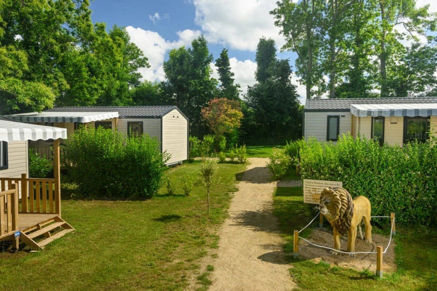 A campsite with two mobile homes, a dirt path, and a lion statue.