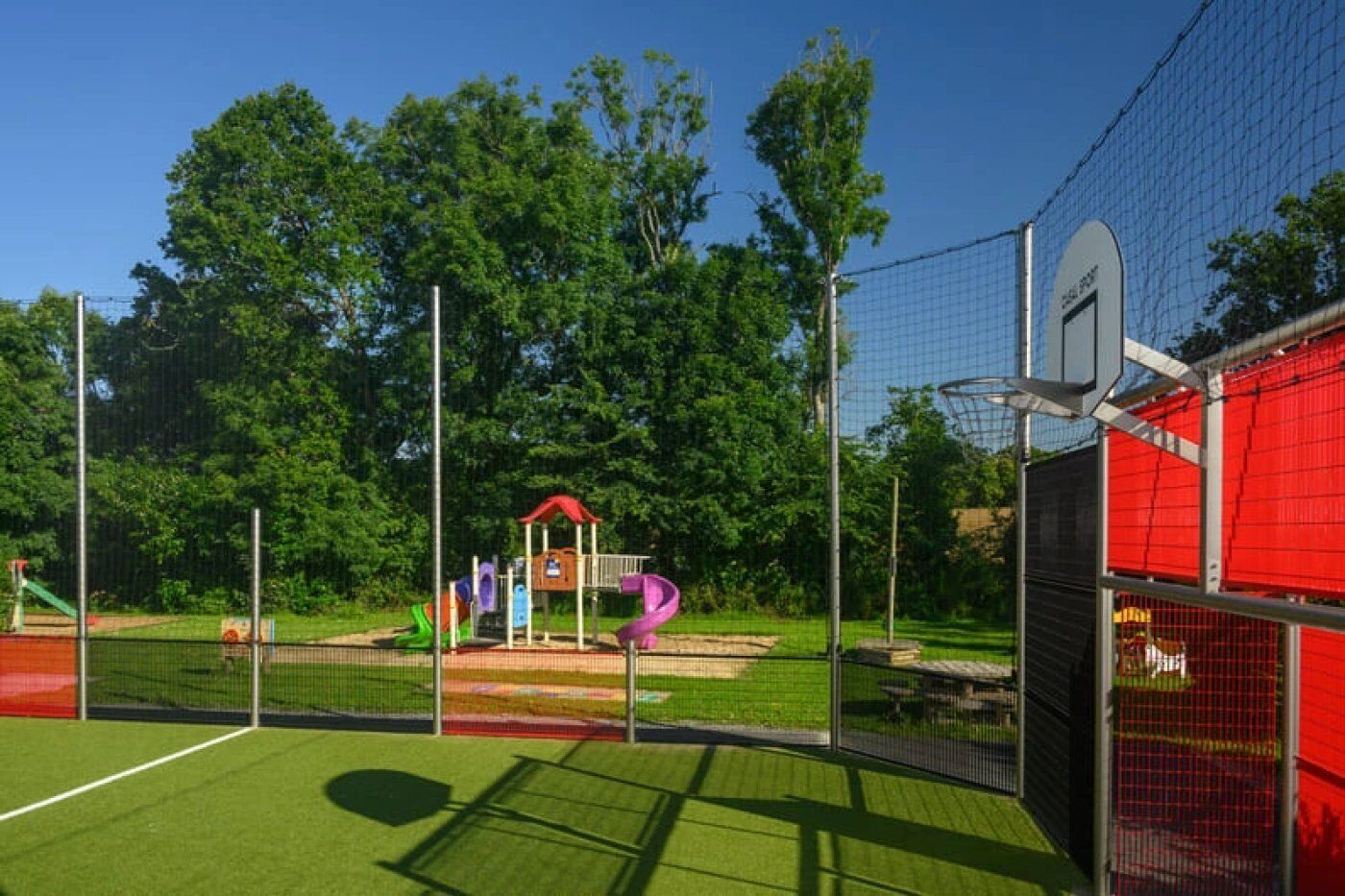 Una cancha deportiva con un aro de baloncesto, un pequeño pabellón y equipo de juegos.