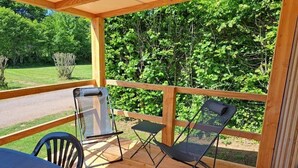 Eine Holzterrasse mit Tisch und Stühlen, eine Glastür und Blick auf eine grüne Landschaft.
