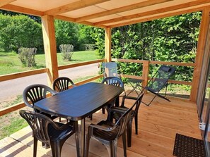 A covered outdoor patio with a wooden table and chairs, surrounded by a wooden railing. - ZEcamping 4 étoiles piscine couverte piscine chauffée locatif TV LV (Pressignac)