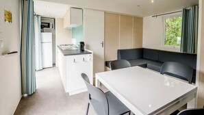 A compact living space with a kitchenette, a dining area, and a seating area with a view of greenery.