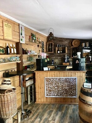 Un rústico área de bar con estantes de madera, mostrador y diferentes botellas y vasos.