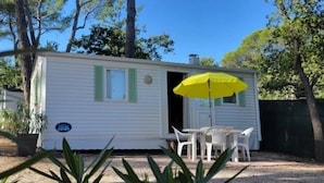 Une petite maison mobile d’un seul étage, avec une porte ouverte, une table entourée de chaises et un parasol jaune.