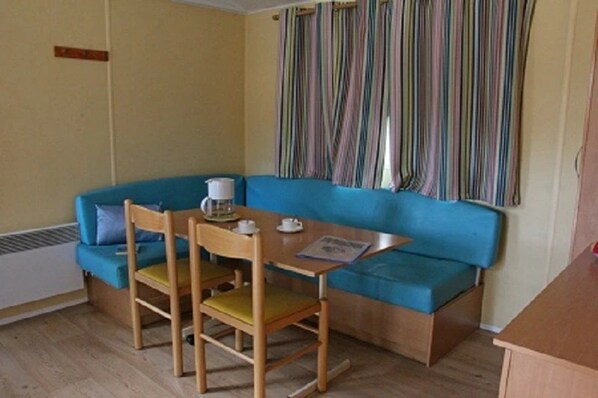 Una habitación con un sofá azul, sillas de madera, una mesita con una taza y un menú, y una cortina a rayas.