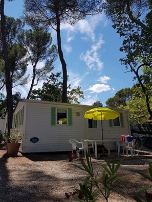 Una casa móvil con un pequeño patio, una sombrilla amarilla y una silla blanca.