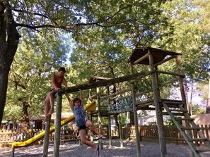 Un parque infantil con una estructura de madera para escalar y un tobogán amarillo.