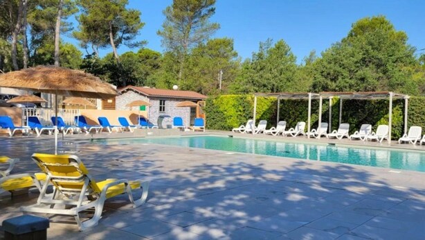 Un espace piscine avec des chaises longues, un coin salon abrité et un bâtiment doté d’un toit de chaume.
