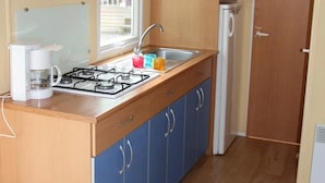 Une cuisine de taille réduite, équipée d’une cuisinière à gaz, d’un évier et de meubles de rangement bleus.