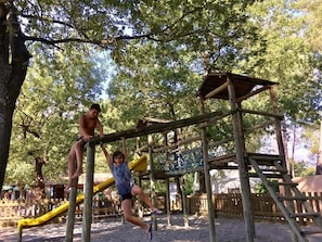 Une aire de jeux avec une structure d’escalade en bois et un toboggan jaune.