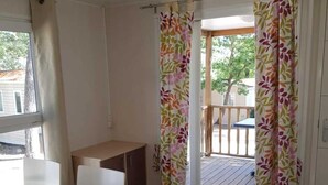 A room with a wooden floor, a desk, a chair, and a view of an outdoor deck with a table and chairs. - ZEcamping 3* toboggans piscine locatif 25m2 4 pers (Peynier)