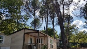 A single-story mobile home with a porch, surrounded by trees. - ZEcamping 3* toboggans piscine locatif 25m2 4 pers (Peynier)