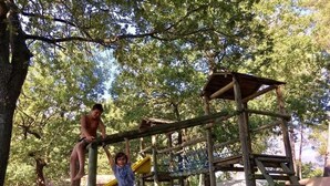 Un parque infantil con una estructura de madera para escalar y un tobogán amarillo.