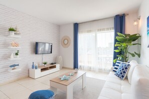 A modern living room with a white brick wall, a flat-screen TV, a white sofa, a coffee table, and a large plant.