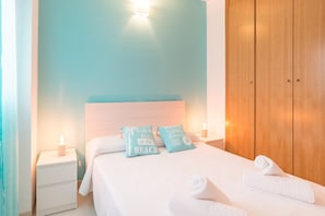 A neatly made bed with two pillows, a nightstand with a lamp, and a wooden wardrobe.