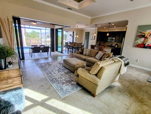 A spacious living room with a large sectional sofa, a dining area, and a kitchen in the background.