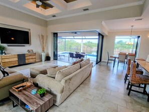 A spacious living area with a large sofa, a coffee table, and a TV. There is a dining area with chairs and a table.