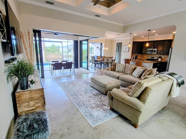 A spacious living area with a large sofa, a coffee table, and a dining table. There is a kitchen area with modern appliances and a dining area with chairs.