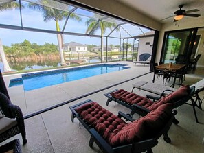 A pool area with lounge chairs, a table, and a view of a lake and houses.