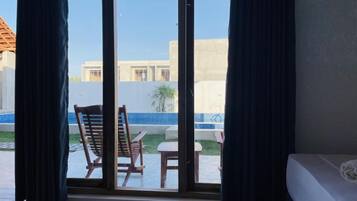 Une chambre avec vue sur une piscine, une chaise en bois et une table à l’extérieur.