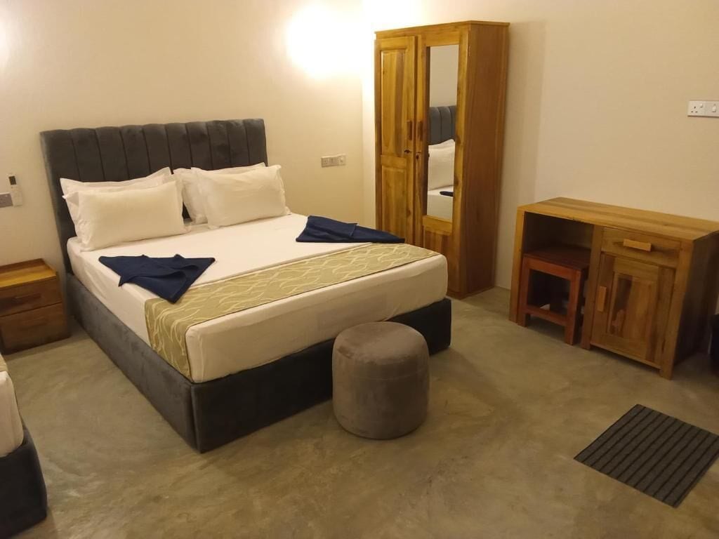 A bedroom with a bed, a wardrobe, a desk, and a small stool.