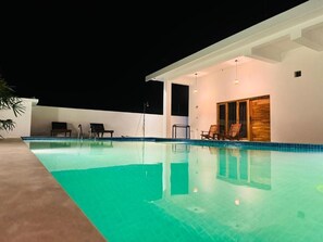 Una piscina con sillas de descanso y un área de estar techada.