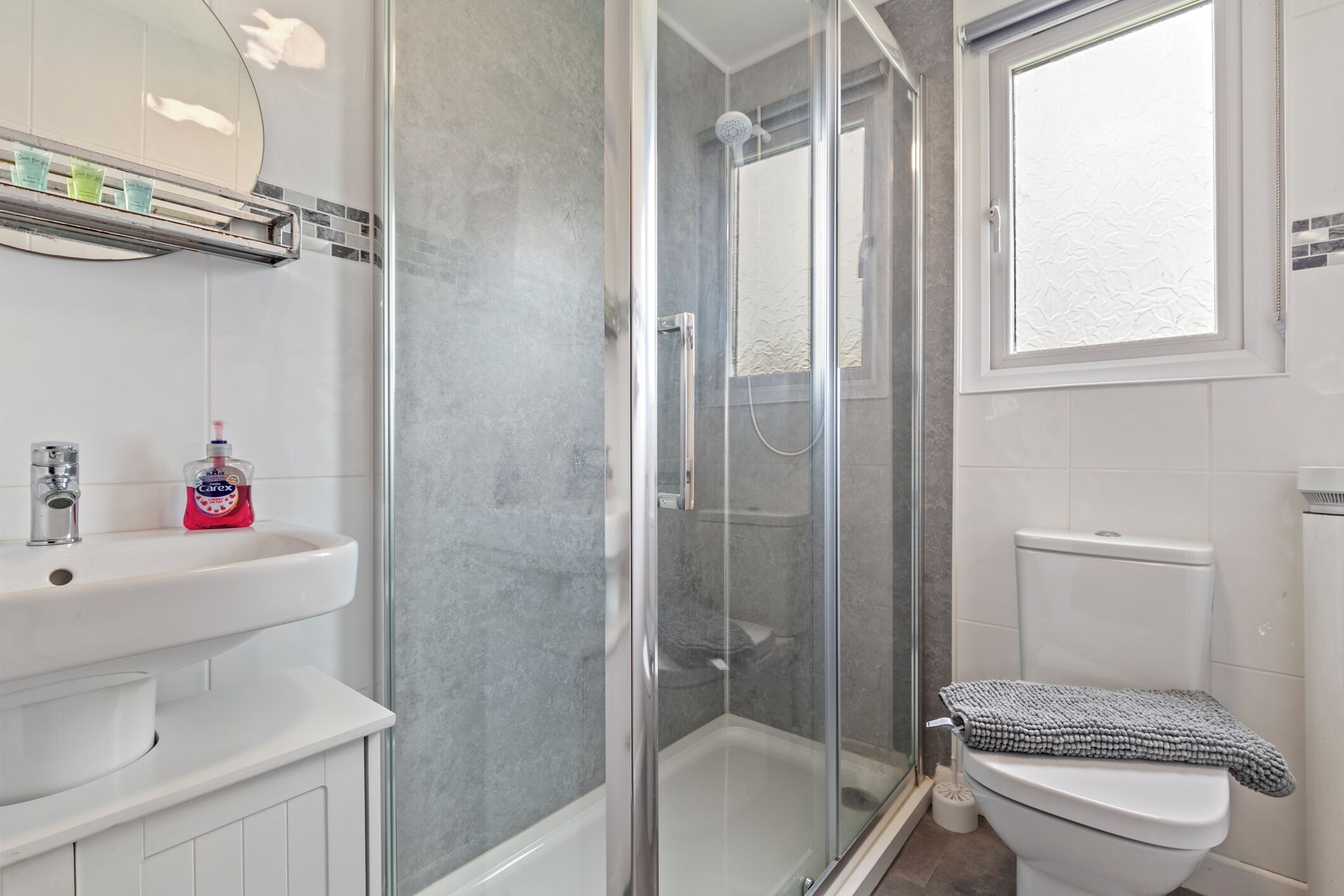 Une salle de bain avec une douche à parois de verre, un lavabo blanc doté d’un distributeur de savon et des toilettes avec une serviette posée sur la lunette.