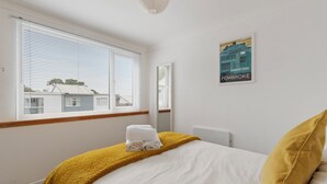 Ein Schlafzimmer mit Bett, einem Fenster mit Jalousien, einem Wandposter und einem Heizkörper.