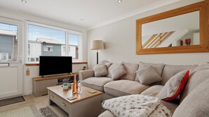 Ein modernes Wohnzimmer mit Flachbildfernseher, einer Couch, einem Couchtisch und einem großen Spiegel.