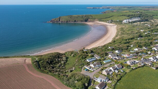Eine Luftaufnahme einer Küstenlandschaft mit Strand, Wohnhäusern und landwirtschaftlichen Feldern.