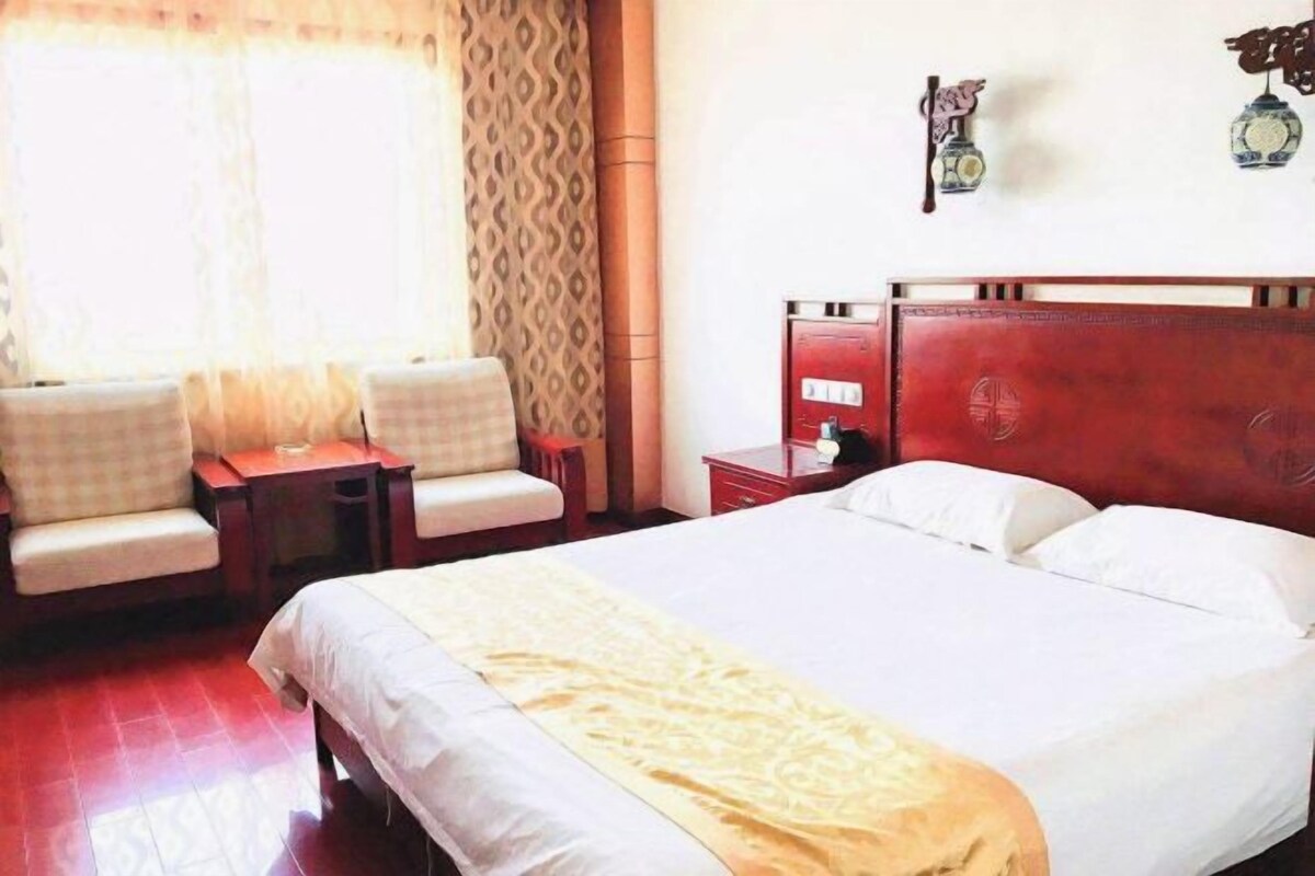 A hotel room with a large bed, a small table, two chairs, a nightstand, and a red headboard.