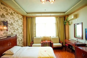 A hotel room with a bed, two chairs, a desk, a mirror, and a window with curtains.