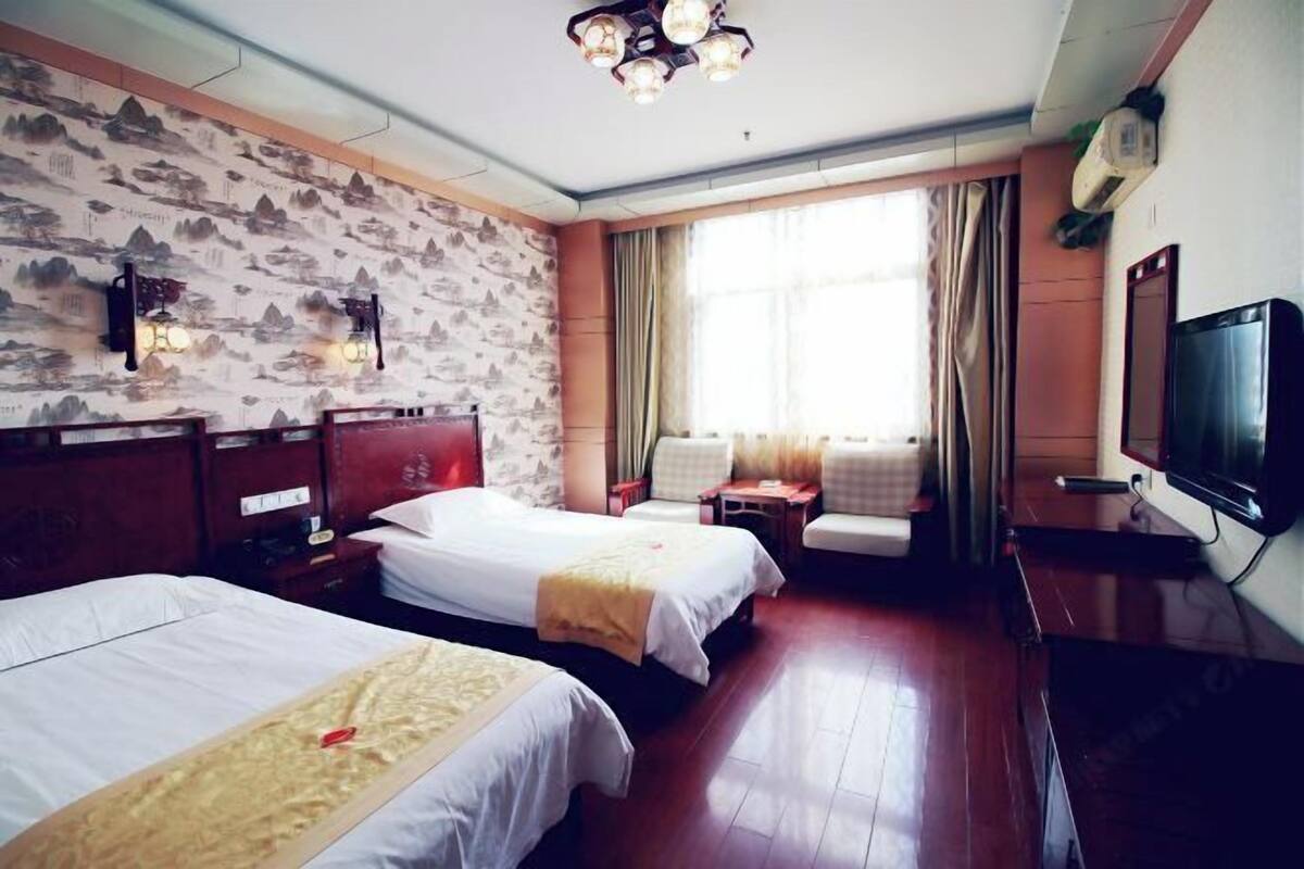 Une chambre d’hôtel avec deux lits, une télévision, un bureau et une fenêtre avec des rideaux.