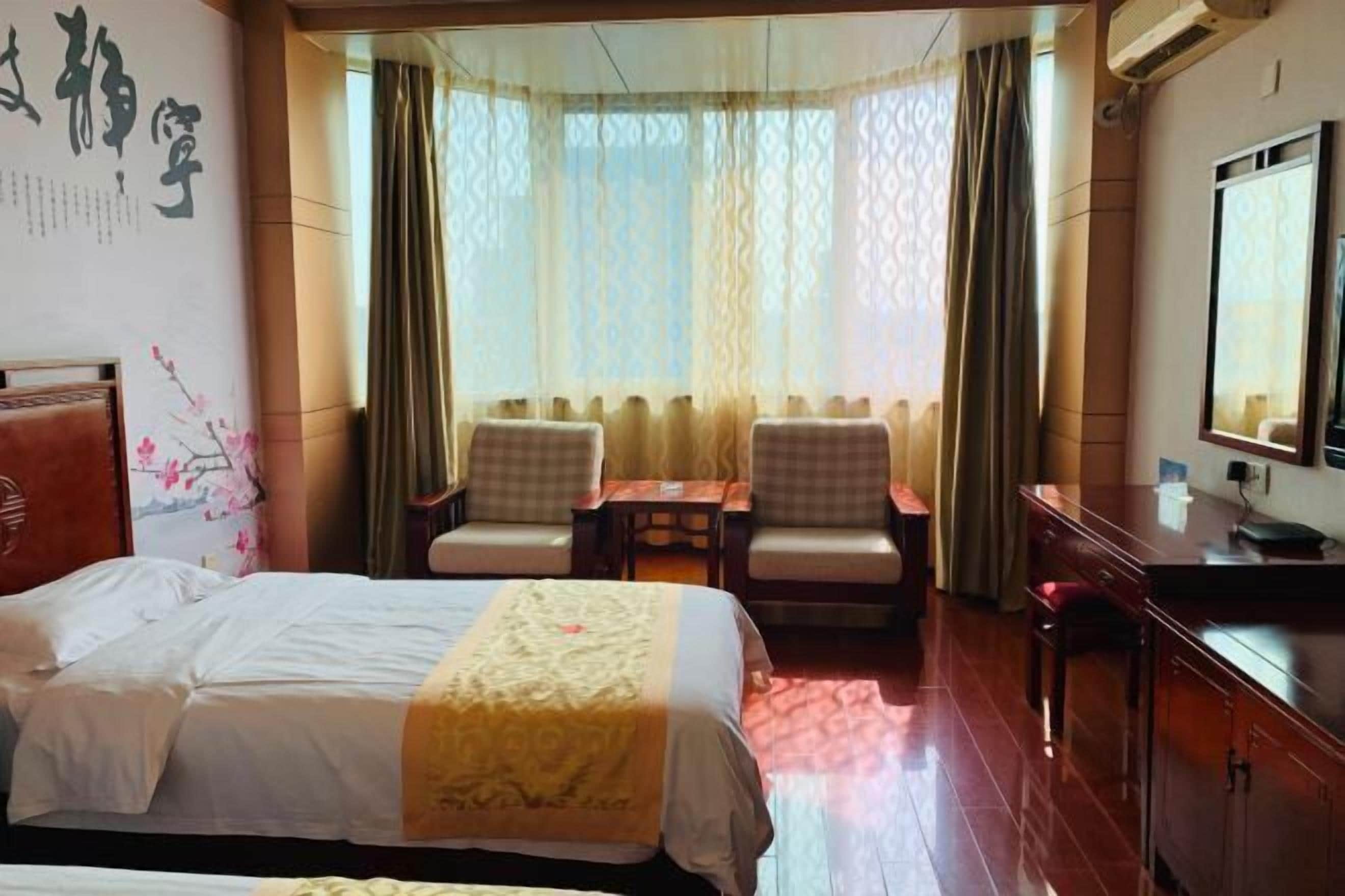 Una habitación de hotel con cama, dos sillas, una mesita, un escritorio y un espejo.